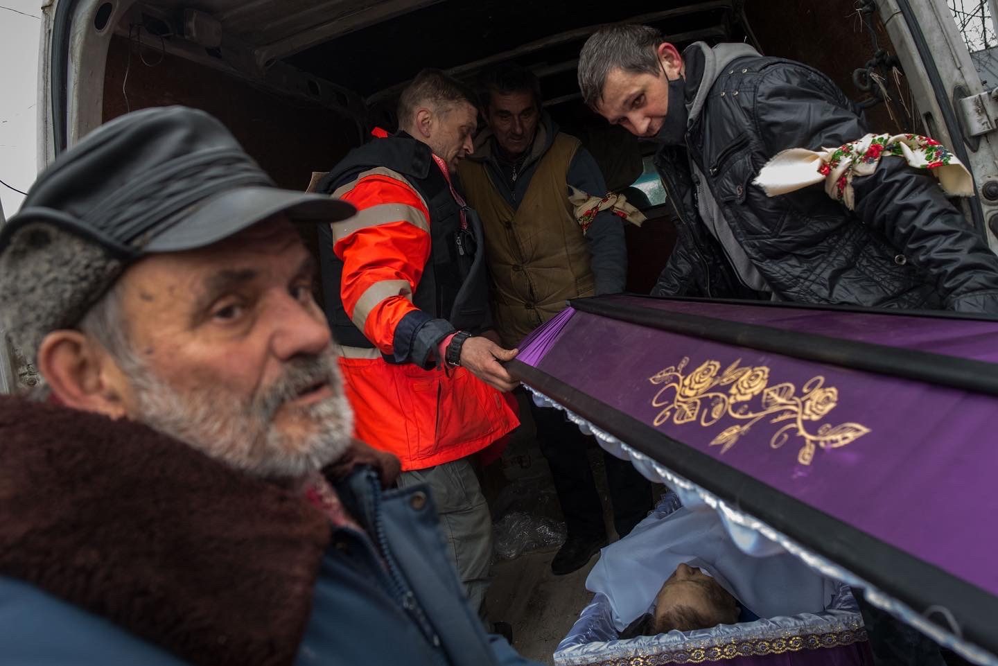 Men lifting a purple coffin out of the back of a van, one in an orange high-visibility vest